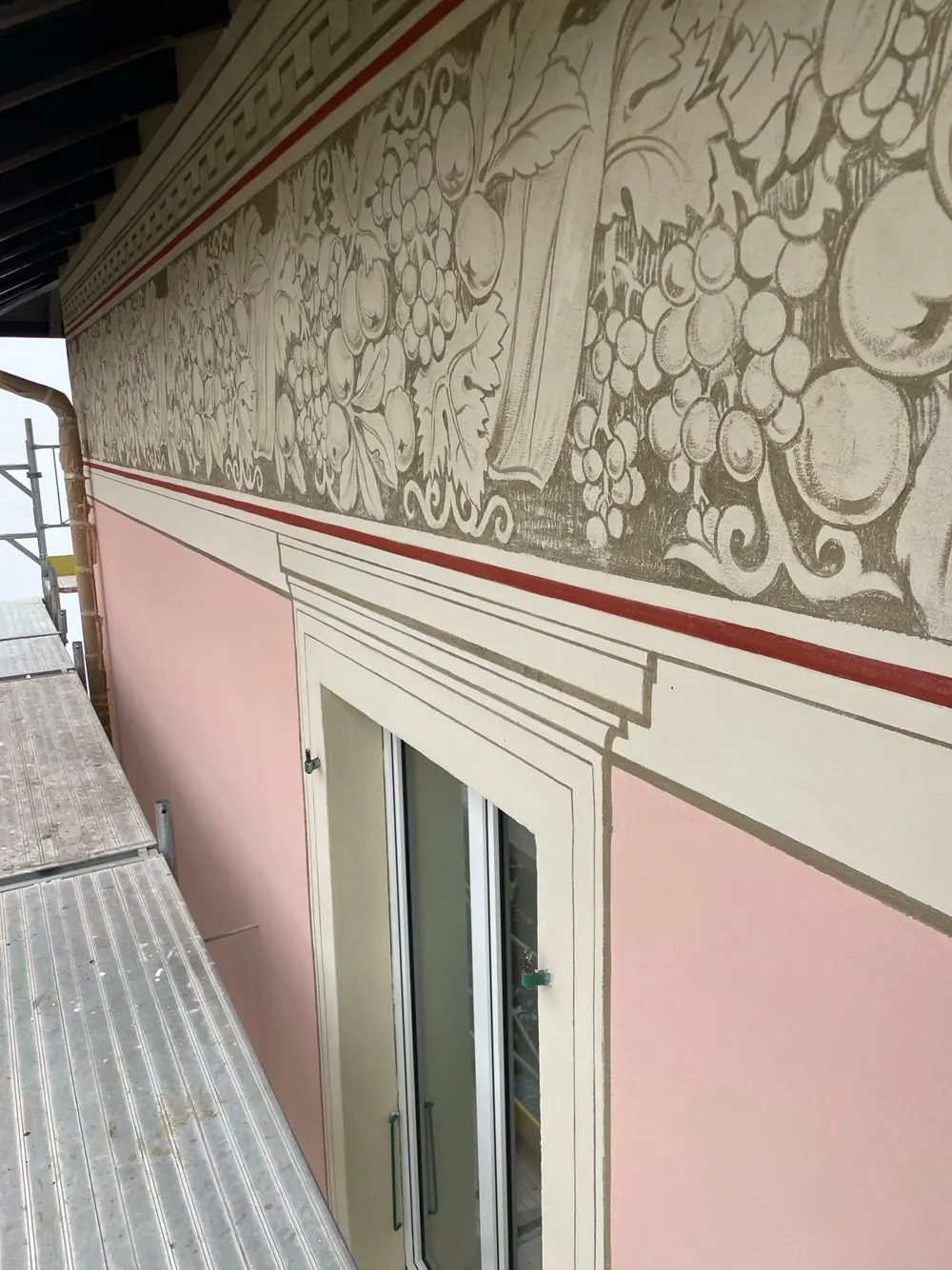 Fregio a sgraffito sopra una finestra su facciata rosa