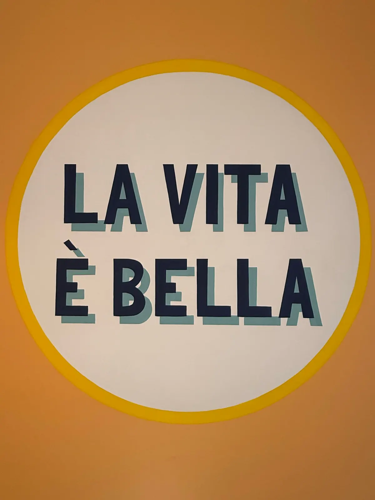 Scritta dipinta «La vita è bella» in un cerchio giallo su fondo arancio