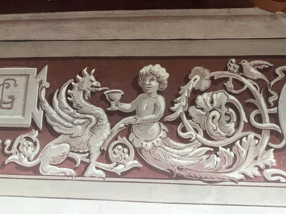 Dettaglio di fregio con putto e grifone dipinti in bianco su fondo rosso